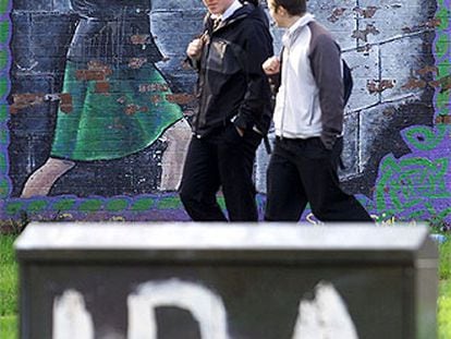 Dos estudiantes caminan entre varias pintadas del IRA en Belfast.