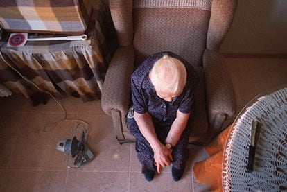 Una anciana aguarda sentada sola en el sillón del salón de su casa.