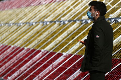 Un hombre con mascarilla ante la bandera gigante de LED en el puente de Juan Bravo en La Castellana de Madrid.