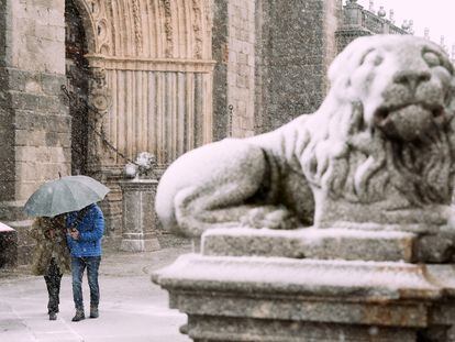 Dos personas se protegen este miércoles de la nieve junto a los leones de la catedral de Ávila.