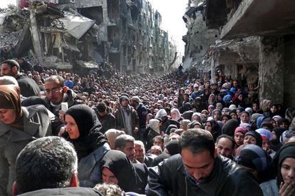 Cientos de personas se agolpan en una calle de Damasco y hacen cola para recibir comida. Son refugiados palestinos del asediado campo de Yarmouk.