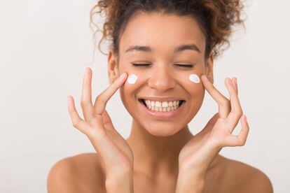 Skin care. Laughing girl applying moisturizing cream on her face over white background