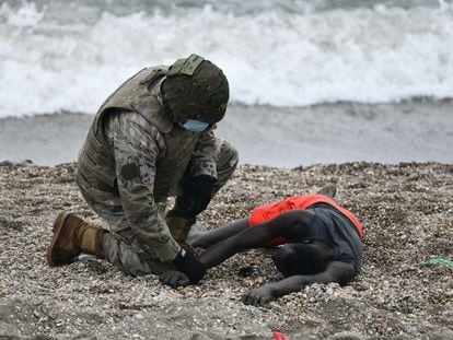 Un militar atiende a una persona tumbada en la orilla de la playa de Ceuta tras haber llegado a nado desde Marruecos, el pasado martes.