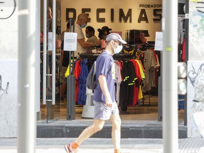Un hombre protegido con mascarilla pasa junto a una tienda en Madrid.