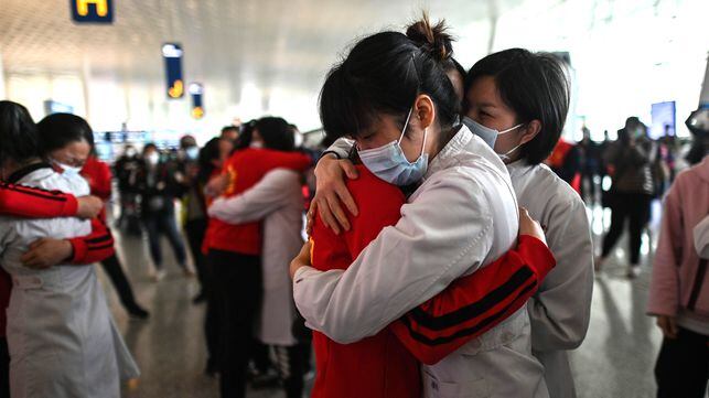 TOPSHOT - Medical staff from Jilin Province (in red) hug nurses from Wuhan after working together during the COVID-19 coronavirus outbreak during a ceremony before leaving as Tianhe Airport is reopened in Wuhan in China's central Hubei province on April 8, 2020. - Thousands of Chinese travellers rushed to leave COVID-19 coronavirus-ravaged Wuhan on April 8 as authorities lifted a more than two-month prohibition on outbound travel from the city where the global pandemic first emerged. (Photo by Hector RETAMAL / AFP)