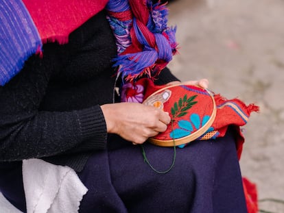 Close-up view of an unrecognizable woman embroidering floral motifs on a maroon textile