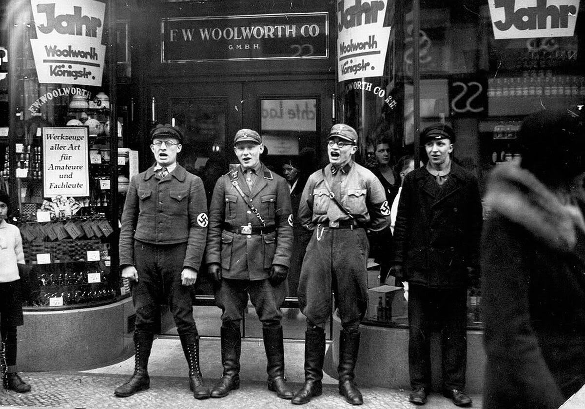 Nazis uniformados cantando ante un comercio judío durante un pogromo.