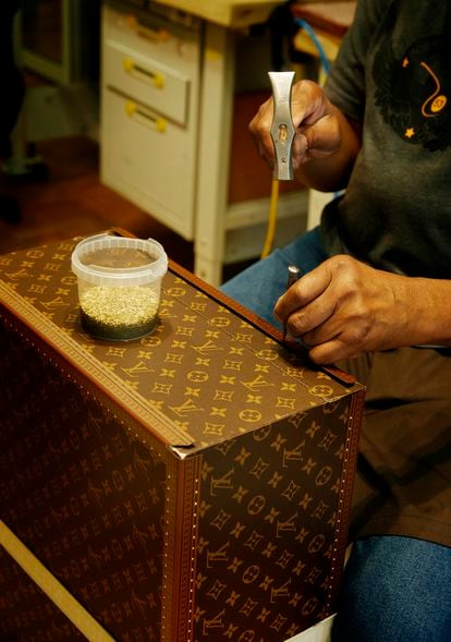 A craftsman places the rivets on the canvas of a trunk.