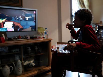 Un niño come un trozo de pizza del menú infantil de Telepizza mientras ve la televisión en su casa, en Usera.