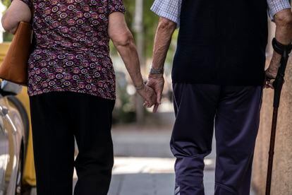 Un hombre y una mujer mayores caminando cogidos de la mano por la calle Caramuel, en el barrio de Puerta del Ángel, Madrid.