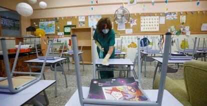 Una limpiadora desinfecta el mobiliario de un colegio.