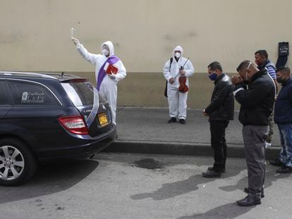 Un clérigo rocía agua bendita mientras familiares se reúnen alrededor del coche fúnebre que transporta a una víctima del COVID-19 al cementerio Chapinero en Bogotá, Colombia, el pasado 6 de agosto de 2020.