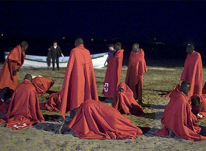 Varios de los 67 pasajeros del cayuco que ha llegado esta madrugada a la playa de Fañabé, en el municipio tinerfeño de Adeje, se cubren con mantas facilitadas por la Cruz Roja.