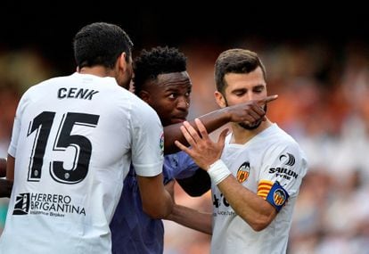 El jugador del Real Madrid Vinicius Junior señala a la grada de los  aficionados del estadio de Mestalla sujetado por los jugadores del Valencia Gaya y Ozkacar, este domingo. 