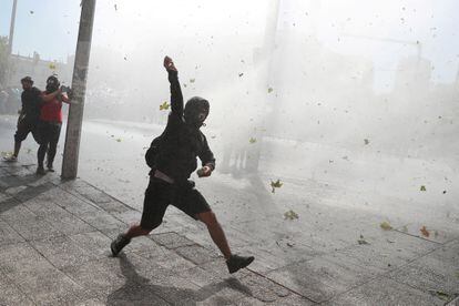 Un manifestante se prepara para lanzar una piedra mientras un coche de la policía antidisturbios lanza un chorro de agua durante protesta estudiantil en Santiago este 25 de marzo.