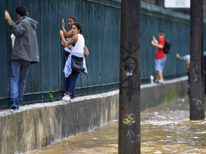 Varias personas se apoyan en una cerca para atravesar una calle inundada.