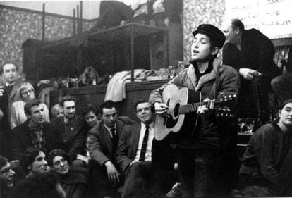 Bob Dylan se mudó de Minneapolis a Nueva York en 1961, cuando tenía 20 años. Frecuentaba los locales 'folk' del barrio bohemio de Greenwich Village ofreciéndose para dar conciertos. Dormía en sofás de la casa de amigos e incluso los dueños de los locales le dejaban pasar la noche allí, una vez que habían cerrado. Una de sus peculiaridades era su poder de fabulación. Llegó a decir que era huérfano y que se había escapado de un circo. También aseguró que era medio sioux, cuando procedía de judíos europeos del Este. “Nadie se lo tenía en cuenta. Reinventarse a uno mismo siempre ha sido parte del mundo del espectáculo. Pero él acababa atrapado en su propia mentira”, dijo el cantante neoyorquino Dave Van Ronk, que ejerció de tutor de Dylan en sus primeros pasos por Greenwich. En la imagen, actuando en el local londinense Singers Club Christmas, en su primera visita a Inglaterra, en 1962.