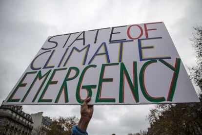 Un activista sujeta un cartel durante la Cumbre del Clima junto del Arco del Triunfo de París en el que se puede leer "Estado de emergencia climática"