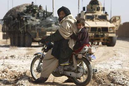 Un afgano y su hijo esperan a que pasen vehículos blindados para cruzar la carretera en la provincia de Helmand (Afganistán).
