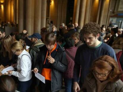 Los ciudadanos escogen las papeletas para ejercer su voto en las elecciones generales, antes de incorporarse a la cola en el colegio electoral situado en la Universitat de Barcelona. EFE/Toni Albir