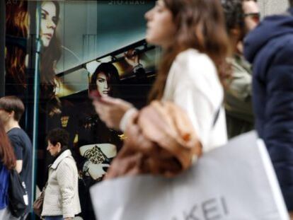 Varias personas pasan con bolsas de compras ante una de las tiendas de la c&eacute;ntrica calle Preciados de Madrid.