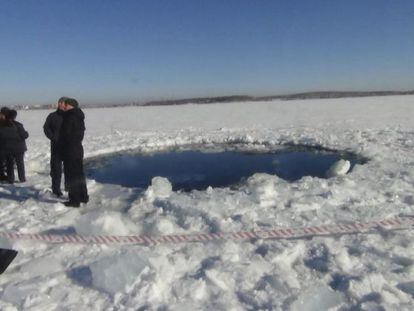 Unos hombres pasean al lado de un agujero de ocho metros en el lugar donde un meteorito impactó, en el lago congelado Chebarkul, Rusia