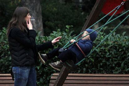 Una mujer fuma muy cerca de un niño en una zona infantil del parque del Retiro, ayer, en Madrid.