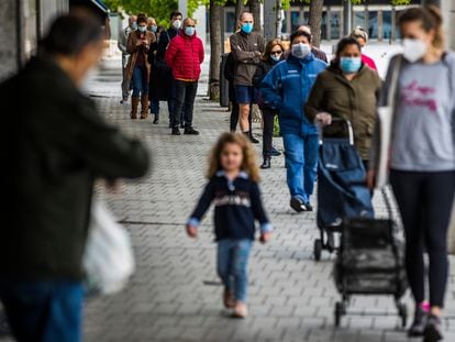 Una madre y su hija esperan en una cola para hacer la compra en Madrid, en una fila de personas protegidas con mascarillas frente al coronavirus.