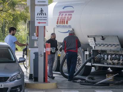 Dos operarios llenan un depósito de carburante de una estación de servicio en Sevilla mientras un cliente reposta.