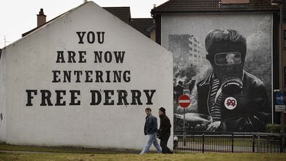Dos personas caminan frente a un cartel en una fachada donde se puede leer "Estás entrando en la Derry libre" en el año 2010.