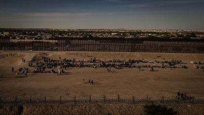 Un grupo de migrantes espera junto al muro fronterizo.