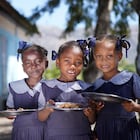 Tres niñas haitianas posan con sus platos de bulgur en su escuela. El Programa Mundial de Alimentos sirve hasta 250.000 menús a diario en las escuelas del país.