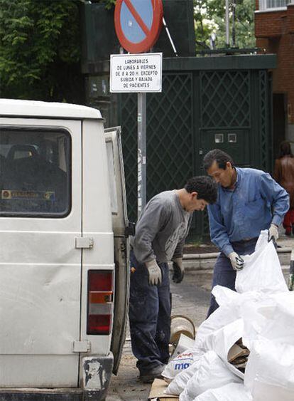 Dos operarios cargan sacos de escombros en una furgoneta