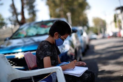 Un estudiante hace los deberes en la calle mientras su madre trabaja en un estacionamiento público, en Ciudad de México.