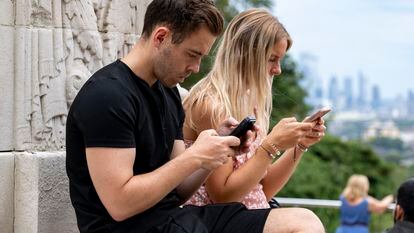 Dos personas utilizan el móvil en un espacio público.