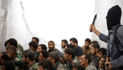 Un miembro del Estado Islámico sostiene un cuchillo junto a un grupo de soldados sirios capturados en Raqqa.