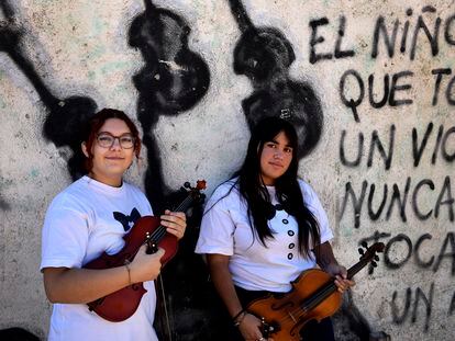 Agustina Llopis y Paloma Tapia frente a un mural de la plaza con una leyenda que da sentido al proyecto: "El niño que toca un violín nunca va a tocar un arma".