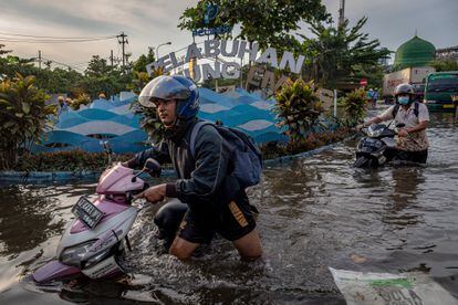 Dos trabajadores empujaban el lunes sus motocicletas a través del agua en un área inundada de la provincia de Java Central, Indonesia.