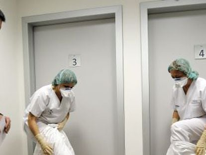 Dos auxiliares del Hospital La Fe (Valencia) se colocan los trajes de protección en presencia de un instructor.