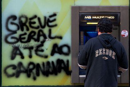 Un cliente usa un cajero en Lisboa, junto a la pintada de una huelga, el pasado noviembre.