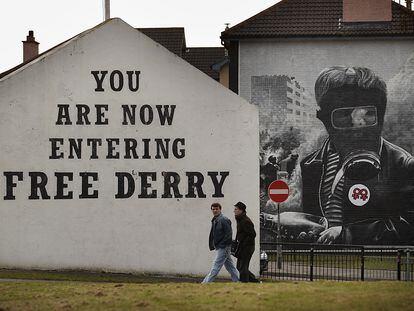 Dos personas caminan frente a un cartel en una fachada donde se puede leer "Estás entrando en la Derry libre" en el año 2010.