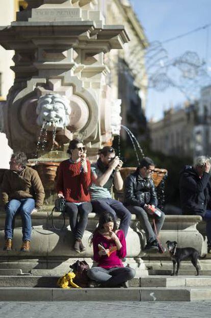 Un grupo de turistas, en una fuente de la Plaza Virgen de los Reyes en Sevilla.
