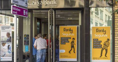 Varios clientes esperan para acceder a una oficina de CaixaBank.
