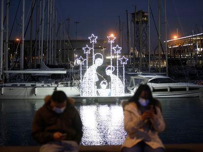 Dos personas junto a un belén luminoso en el puerto de Barcelona, este miércoles.