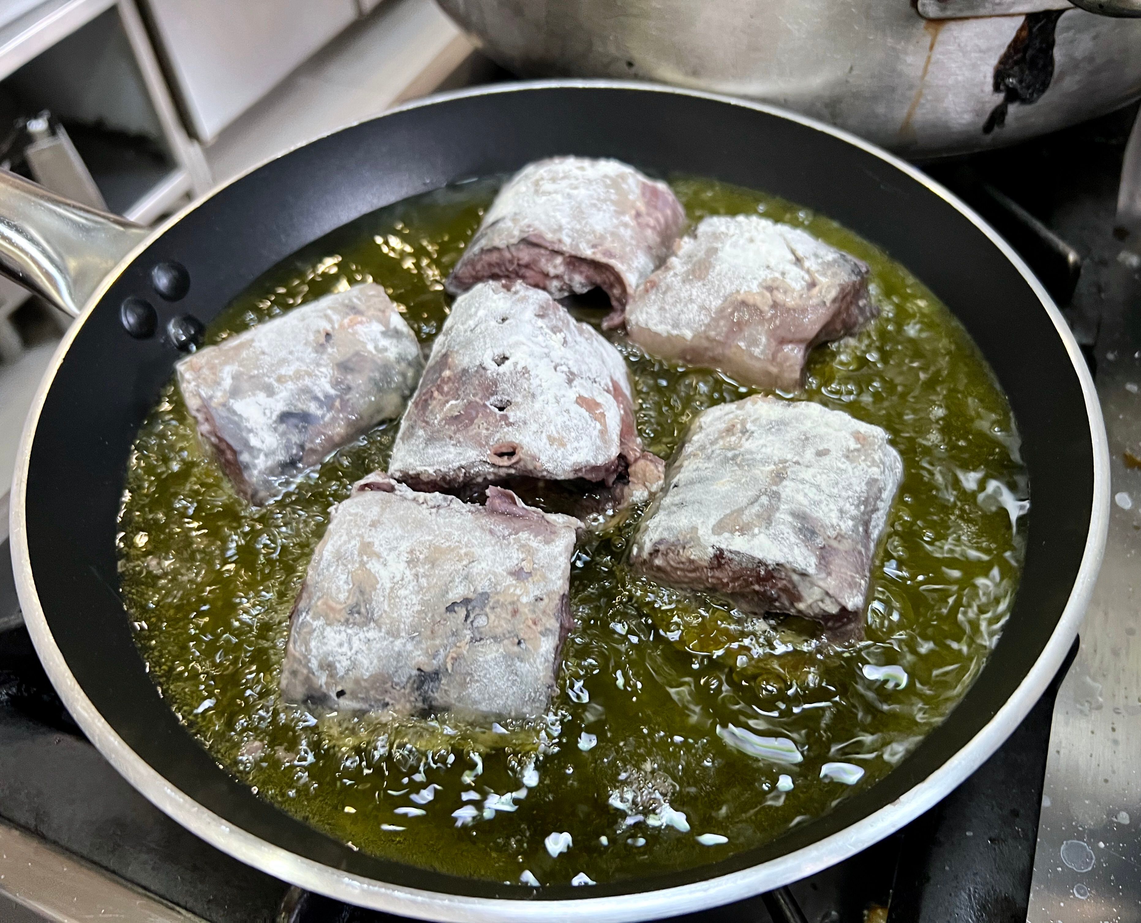 Porciones de lamprea rebozadas en harina friéndose en la sartén. 