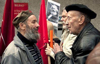 Dos manifestantes charlan con una foto de Karl Marx detrás, momentos antes de comenzar en Bilbao la concentración de protesta
