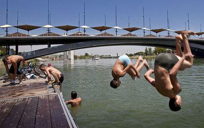 Un grupo de chicos se bañan en la dársena del Guadalquivir, bajo el puente del Cachorro, para intentar sofocar las altas temperaturas registradas en la capital andaluza