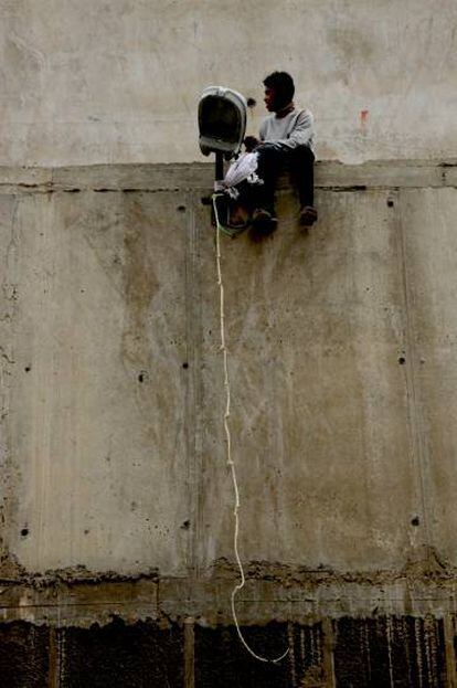 Un joven, sentado junto a una farola con una cuerda en lo alto de un muro del recinto portuario, esperando para saltar.