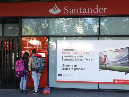 Dos personas retiran dinero de un cajero automático de Madrid junto a un anuncio de hipotecas, en una imagen de archivo.