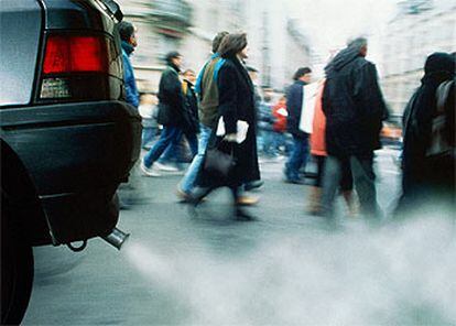 Peatones junto a un vehículo que emite gran cantidad de humo y sustancias contaminantes.